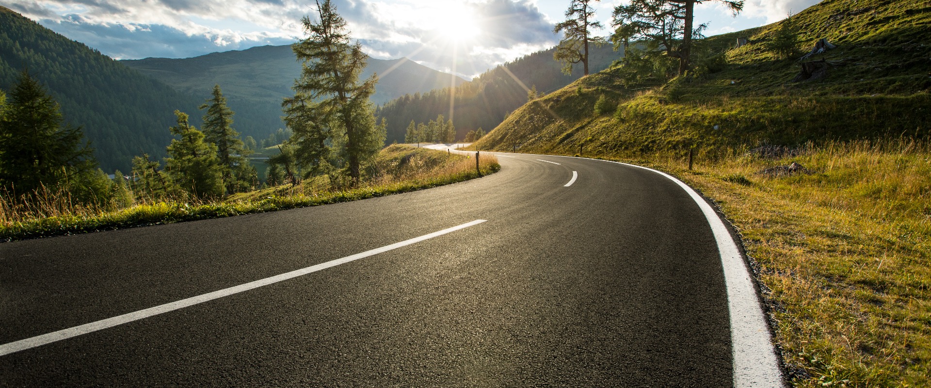Eine Asphaltstraße in Österreich, die Alpen an einem Sommertag.
